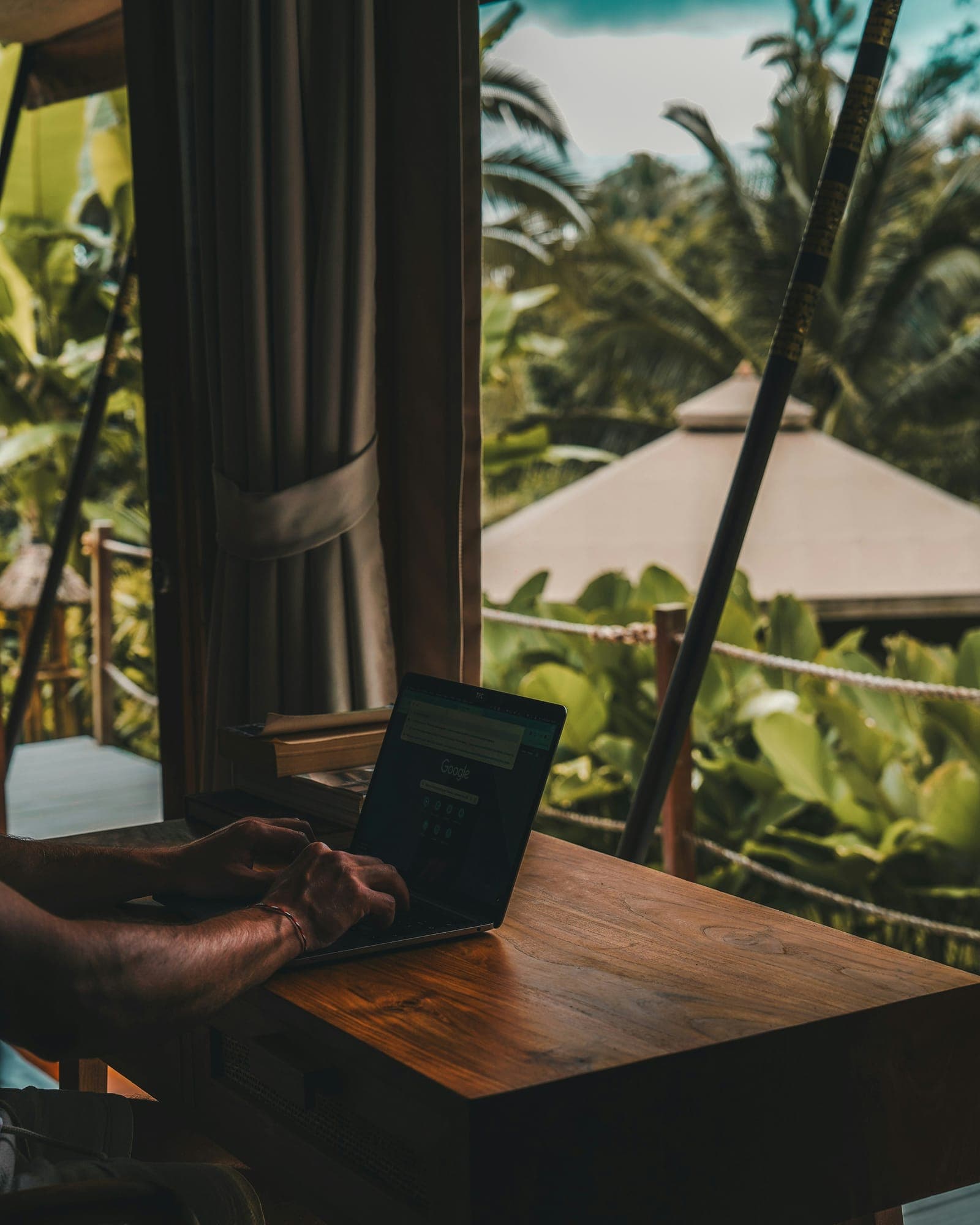 A laptop on a wooden table in an open pavilion, looking out over tropical gardens in Bali